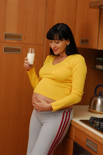 Mujer embarazada joven bebiendo leche en una cocina —  Fotos de Stock