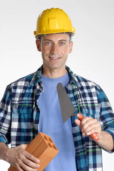 Homem de construção segurando um tijolo de parede e espátula no fundo branco . — Fotografia de Stock