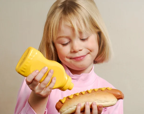 Mladá dívka odlévání hořčice na její hot dog. — Stock fotografie