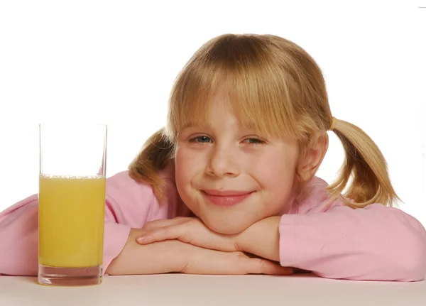 Piccola ragazza bionda dietro un bicchiere di succo d'arancia — Foto Stock