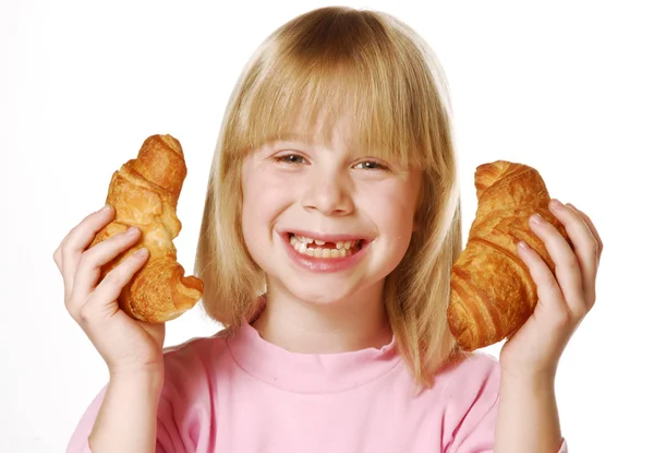 Liten flicka håller och äter croissant. — Stockfoto