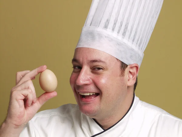 Jeune chef tenant un œuf frais sur fond jaune . — Photo