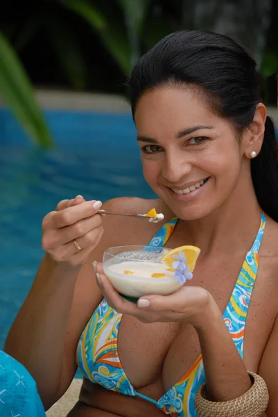 Jovem mulher comendo atrás de uma piscina . — Fotografia de Stock