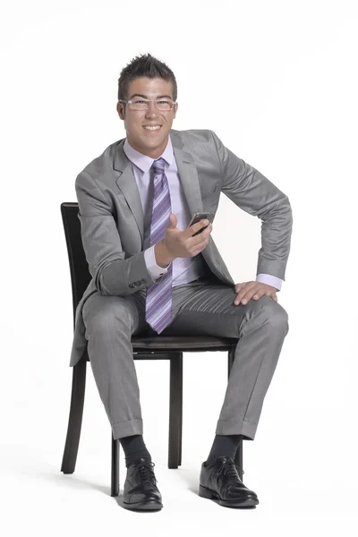 Joven hombre de negocios sentado en una silla y usando un teléfono móvil . — Foto de Stock