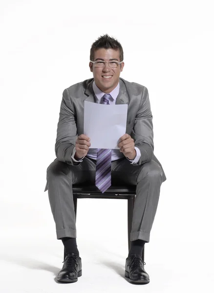 Joven hombre de negocios sentado en una silla y sosteniendo un documento sobre fondo blanco . —  Fotos de Stock