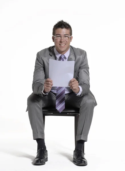 Joven hombre de negocios sentado en una silla y sosteniendo un documento sobre fondo blanco . — Foto de Stock