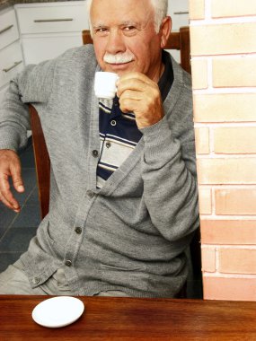 Grand father drinking coffee in a kitchen. clipart