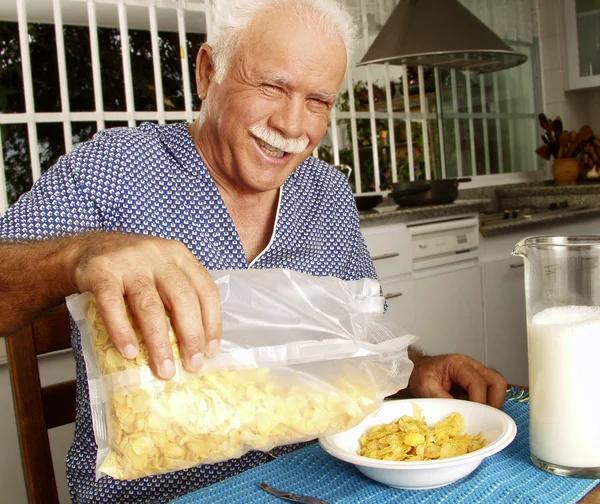 Dziadek jeść płatki kukurydziane zbóż w kuchni. — Zdjęcie stockowe