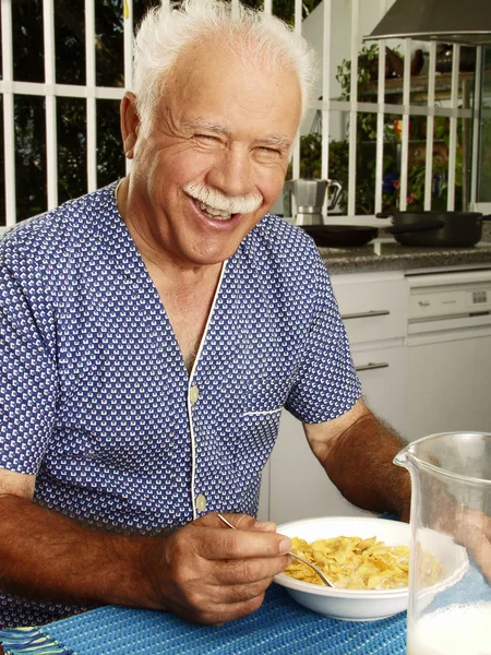 Dziadek jeść płatki kukurydziane zbóż w kuchni. — Zdjęcie stockowe