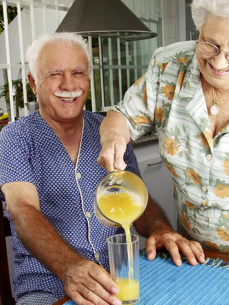 Grand föräldrar dricka och hälla apelsinjuice på kök. — Stockfoto