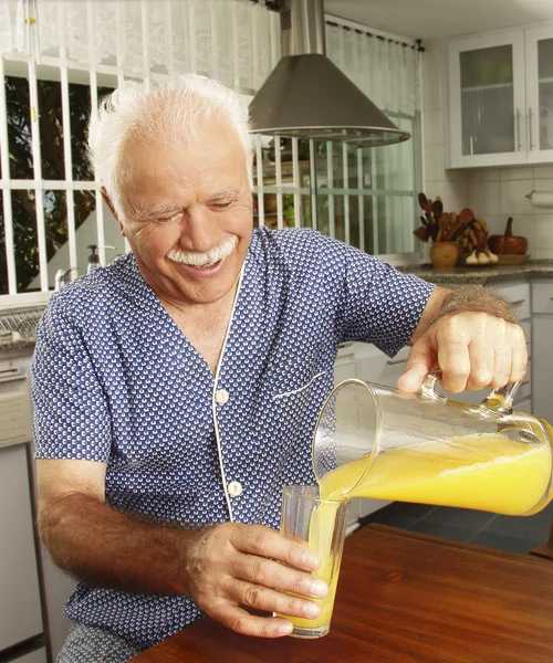 Grand parents drinking and pouring orange juice at kitchen. — Stock Photo, Image