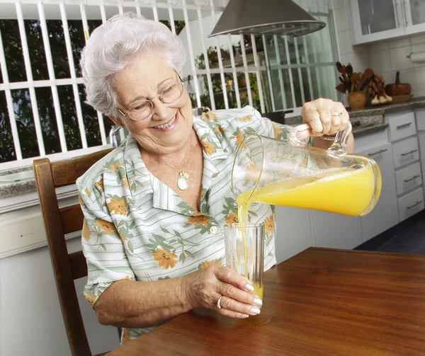 Grandmother drinking orange juice at kitchen. — Stock Photo, Image
