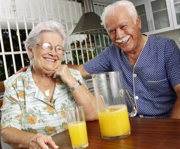 Grand ouders drinken en gieten sinaasappelsap in kitchen. — Stockfoto