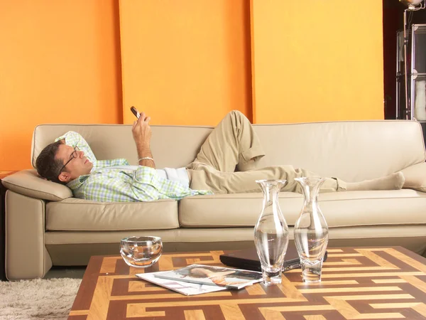 Relaxado jovem deitado no sofá com um telefone mobil . — Fotografia de Stock
