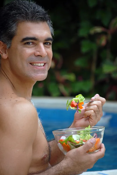 Junger Mann isst Gemüse hinter einem Swimmingpool. — Stockfoto