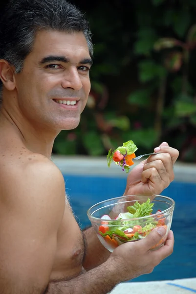 Junger Mann isst Gemüse hinter einem Swimmingpool. — Stockfoto