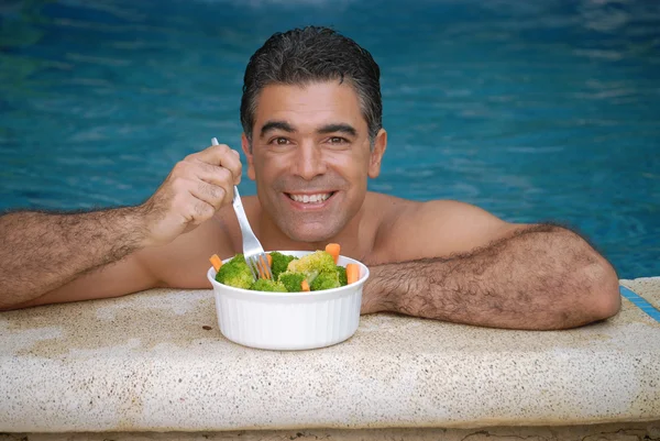 Young man eating vegetable salad in a swimming pool. — Stock Photo, Image