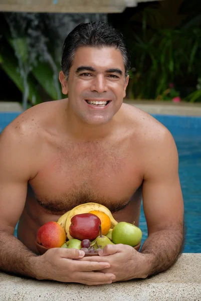 Jeune homme mangeant des fruits tropicaux dans une piscine . — Photo