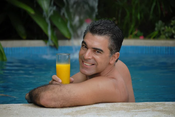 Junger Mann trinkt Orangensaft im Schwimmbad. — Stockfoto