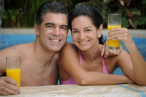 Junges lateinisches Paar trinkt Orangensaft in einem Schwimmbad. — Stockfoto