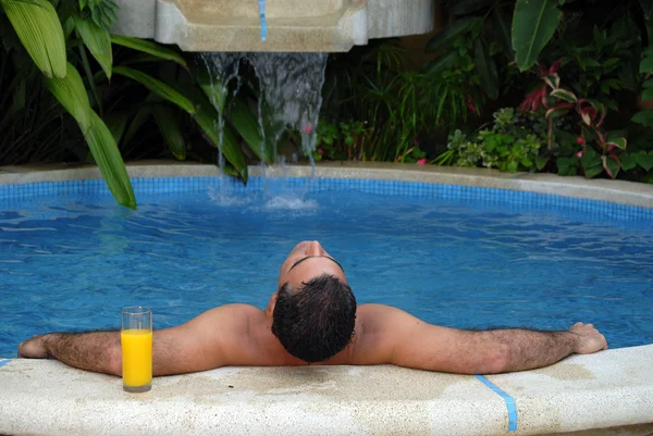 スイミング プールでオレンジ ジュースを飲む若い男. — ストック写真