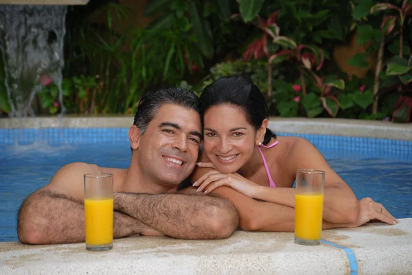Junges lateinisches Paar trinkt Orangensaft in einem Schwimmbad. — Stockfoto