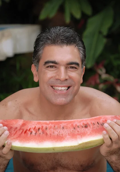 Junger Mann isst eine große Wassermelone in einem Swimmingpool. — Stockfoto