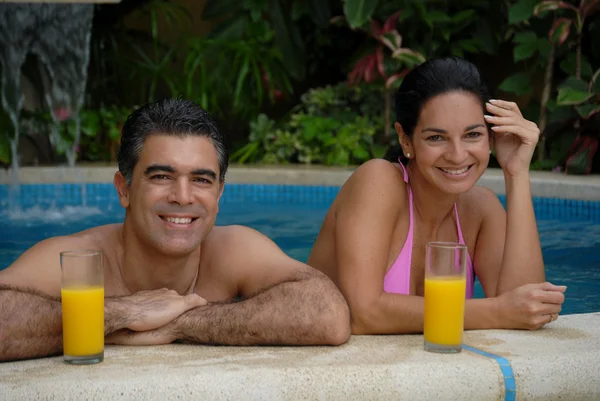 Junges lateinisches Paar trinkt Orangensaft in einem Schwimmbad. — Stockfoto