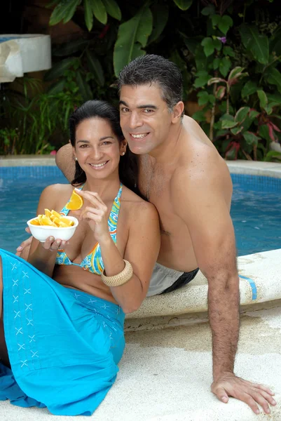 Casal jovem comendo fatias de laranja atrás de uma piscina . — Fotografia de Stock