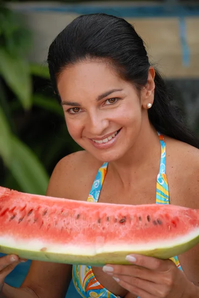 Jonge vrouw eten een grote water meloen in een zwembad. — Stockfoto
