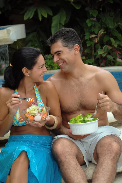 Casal jovem comendo salada atrás de uma piscina . — Fotografia de Stock