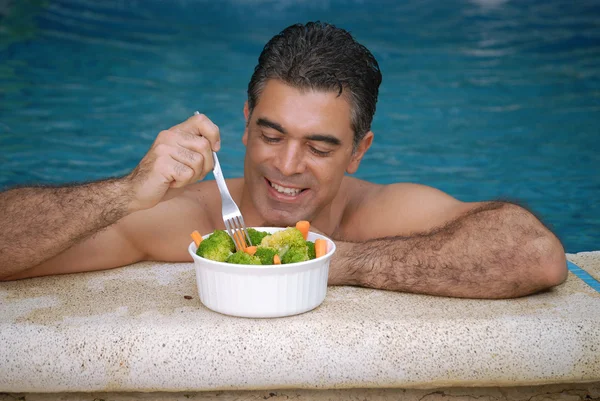 Ung man äta grönsaker bakom en pool. — Stockfoto