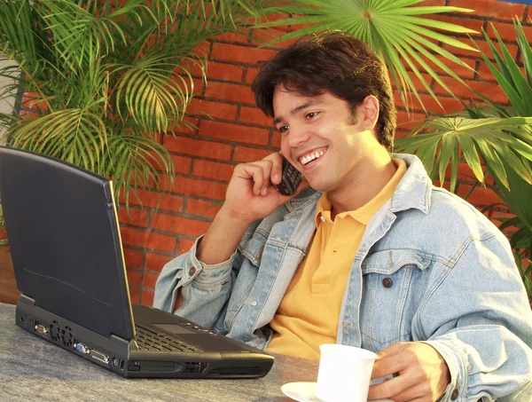 Jovem usando um laptop e conversando em um telefone celular . — Fotografia de Stock