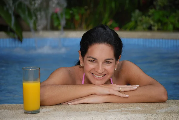 Hispánský žena relaxaci v bazénu a oranžové sklo šťávy. — Stock fotografie