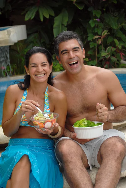 Junges Paar isst Salat hinter einem Swimmingpool. — Stockfoto