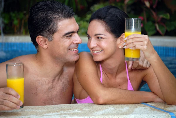 Jovem casal latino bebendo suco de laranja em uma piscina . — Fotografia de Stock
