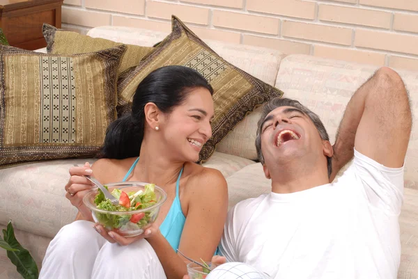 Mitte erwachsenes Paar essen und teilen in einem Wohnzimmer. — Stockfoto