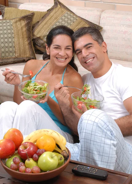 Mid volwassen paar salade en fruit eten in een woonkamer. — Stockfoto