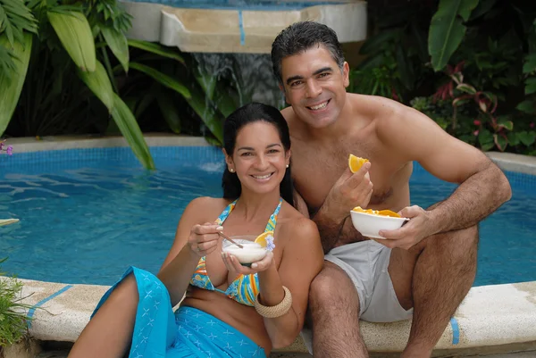 Junges Paar isst Orangenscheiben hinter einem Swimmingpool. — Stockfoto