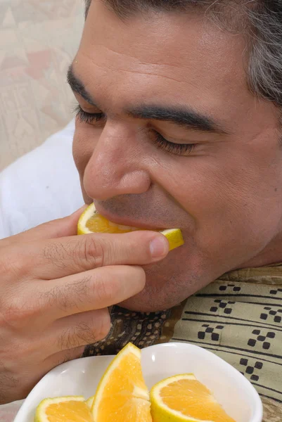 Medio volwassen man oranje segmenten te eten in een bank. — Stockfoto