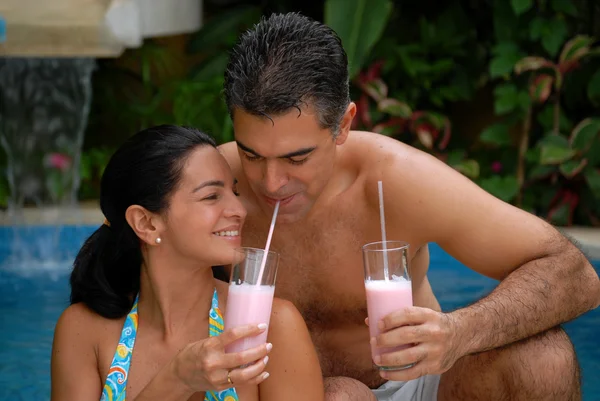Lateinisches Paar trinkt Erdbeer-Milchshake im Schwimmbad. — Stockfoto
