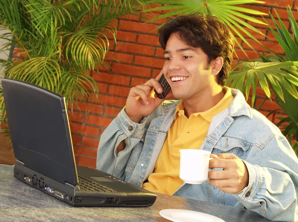 Jovem usando um laptop e conversando em um telefone celular . — Fotografia de Stock