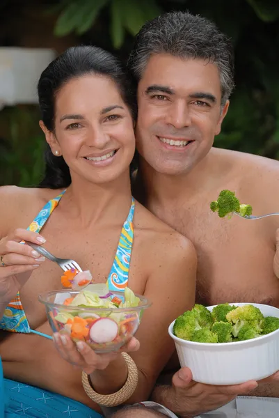 Casal jovem comendo salada atrás de uma piscina . — Fotografia de Stock