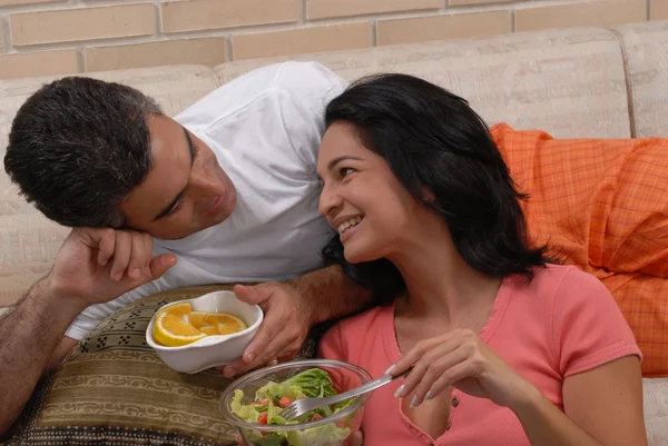 Mid adult couple eating salad and fruit in a living room. — Stock Photo, Image