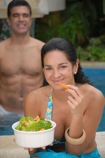 Young couple eating salad behind a swimming pool. — Stock Photo, Image