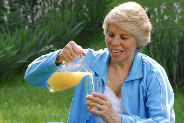 Mujer adulta bebiendo jugo de naranja. Mujer adulta que sostiene naranjas frescas . —  Fotos de Stock