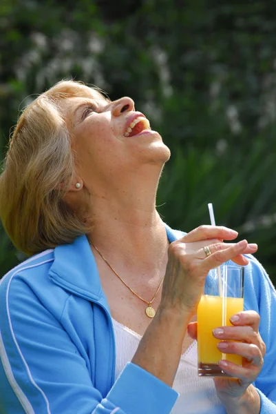 Mid adult woman drinking orange juice. Mid adult woman holding fresh oranges. — Stock Photo, Image