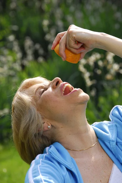 Mid adult woman squeezing an orange in her mouth. — Stock Photo, Image