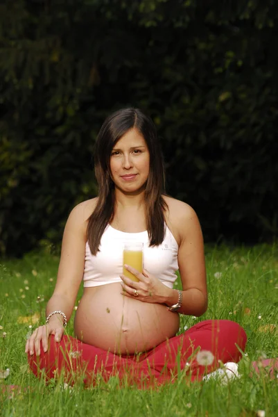 Schöne schwangere Frau trinkt Orangensaft und entspannt sich im Park. — Stockfoto