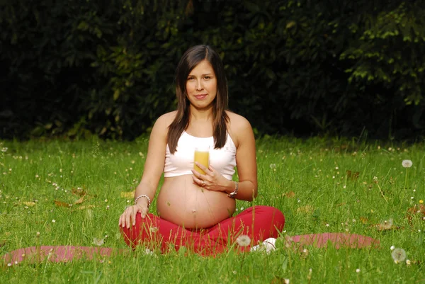 Portakal suyu içme ve rahatlatıcı parkta güzel bir hamile kadın. — Stok fotoğraf
